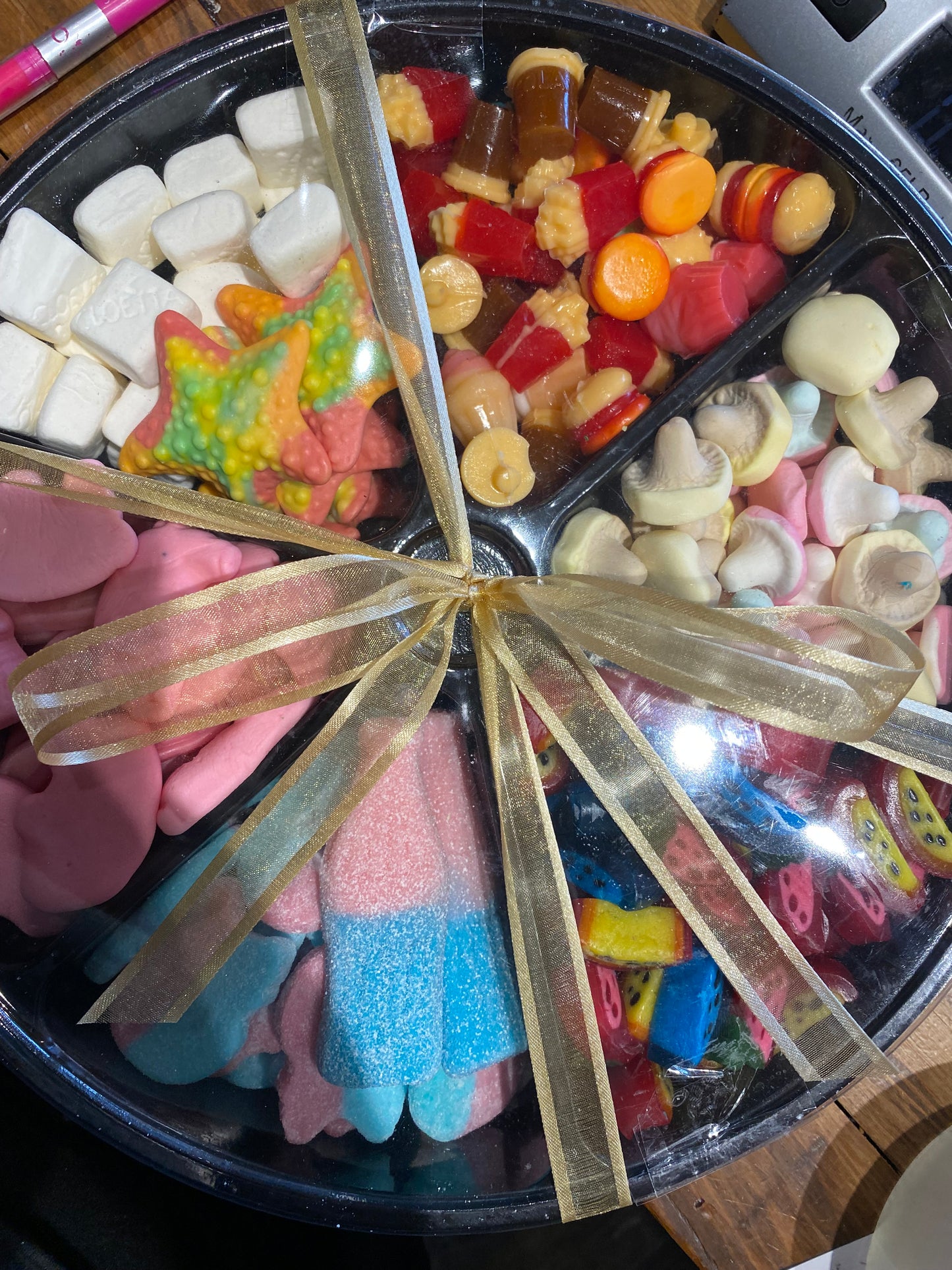 Assorted colorful candies in a round tray with a gold ribbon